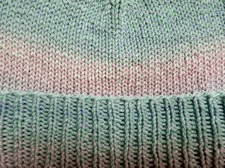 A closeup of the 1x1 rib brim, and the stockinette stitch body, with blue fading into pink