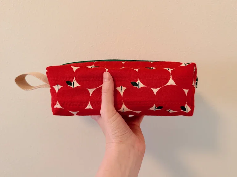 My hand holding the app pouch on its side to show a loop handle of natural-colored webbing