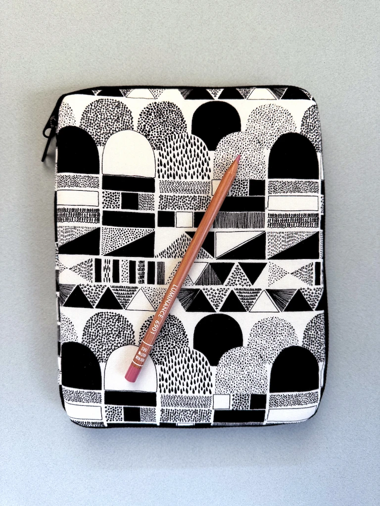A rectangular, puffy case made in black and white patterned fabric featuring shapes with different dotted fills. There is a black zipper zipped around the case.