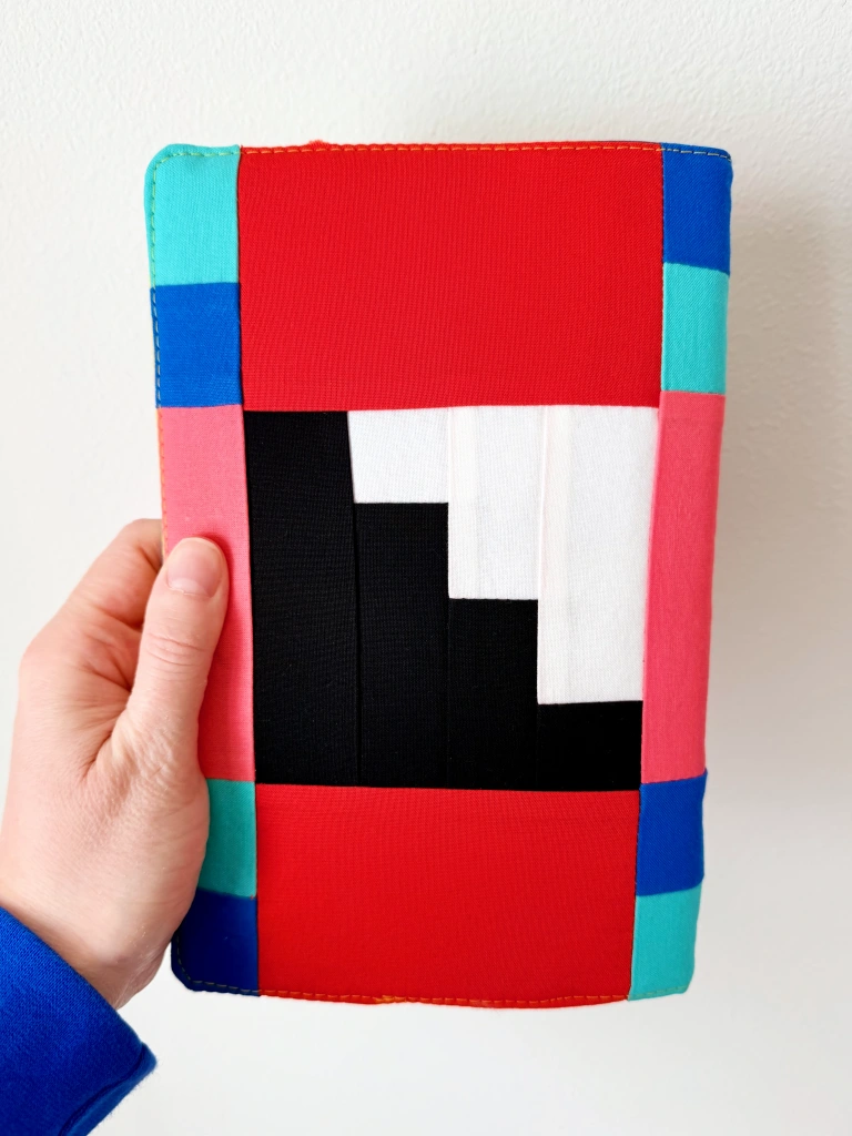 The back central block has a geometric black staircase-looking shape on a white background. Red, pink, blue, and teal rectangles surround the central block.