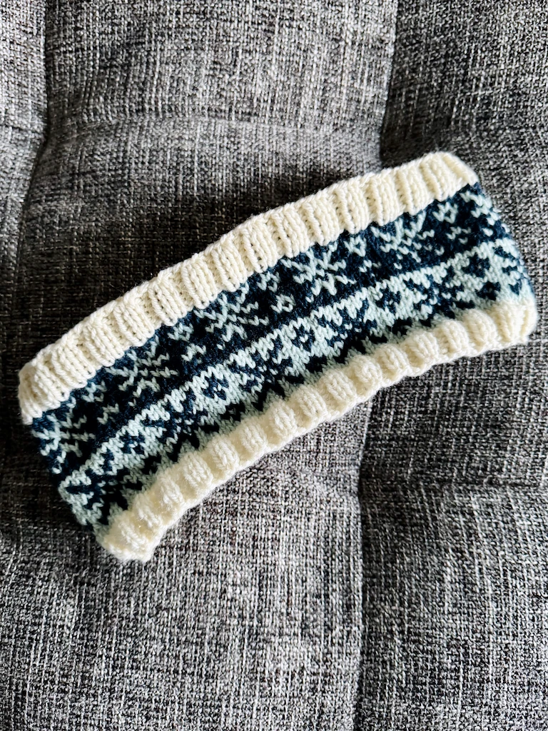 The unfolded headband lying on a grey couch at a jaunty angle. A few of the light blue stitches in the dark blue band look smaller than the others.