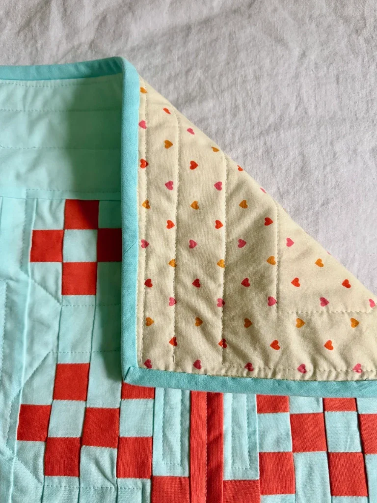 The corner of the quilt flipped over to show the backing fabric: a cream cotton with orange, yellow, and pink hearts.