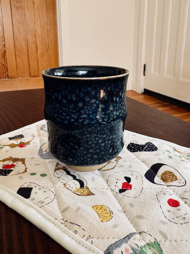 A small, indigo-colored Japanese tea mug on one of the mug rugs. It has no handle, and the glaze has a subtle dappled pattern.