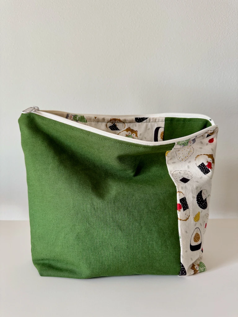 The pouch is unzipped to show that the lining is mostly the hamster fabric, with a narrower strip of green canvas (inverse of the outside)