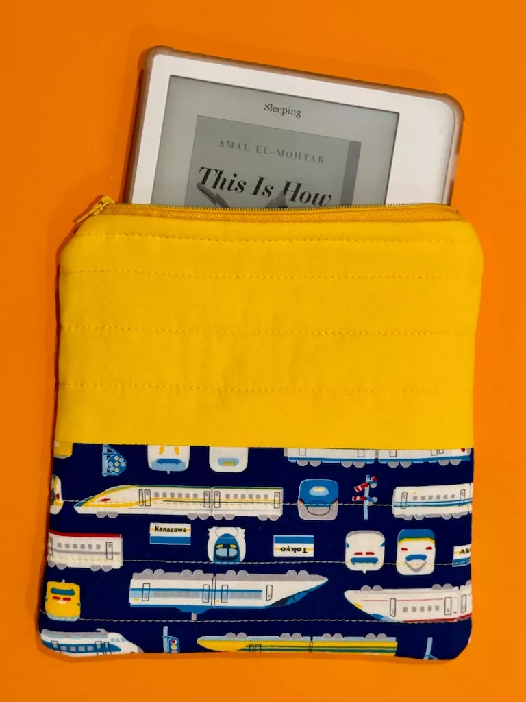 A Kobo peeks out the top of the pouch, against a bright orange background