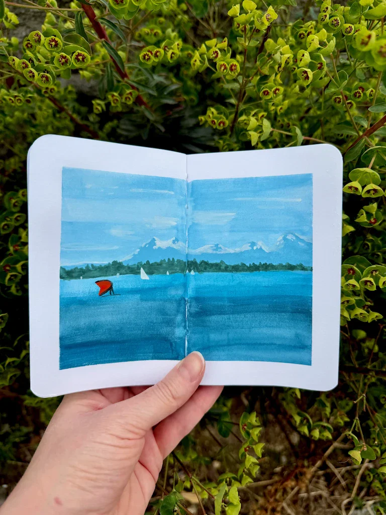 A very blue painted scene featuring the Olympic mountains with a dusting of snow on top. The sky is blue with streaks of clouds. In the foreground is the Puget Sound in swipes of darker blue, a red parasail, and white sails in the further distance.