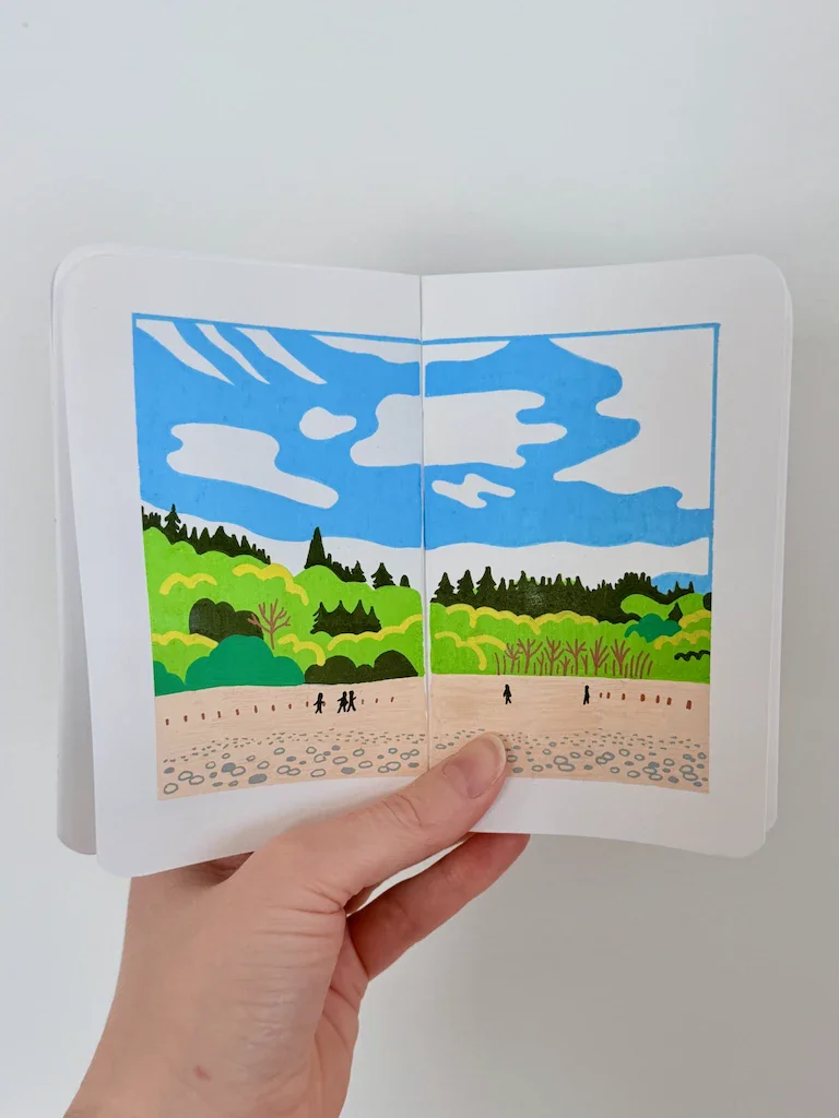 A small sketchbook featuring a bright, graphic landscape. In the foreground is a stony beach with small figures walking in the distance. Beyond that is a hill jampacked with conifers and deciduous trees, and a bright blue sky with bubbly clouds.
