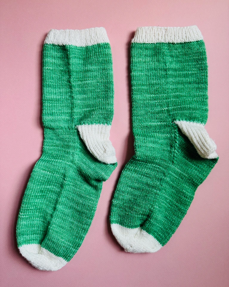 The pair of socks laying on a pink background. They look a bit lumpy, and there's a crease on the side